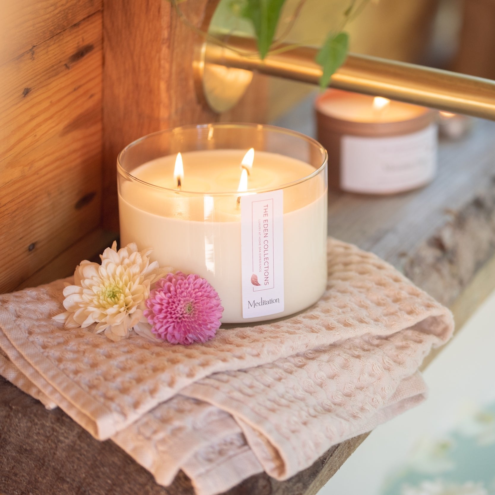 Elegant soy wax candle in a glass jar with three wicks. Scented with essential oil, hand poured by The Eden Collections. Product photography was taken in a beautiful bathroom with flowers.