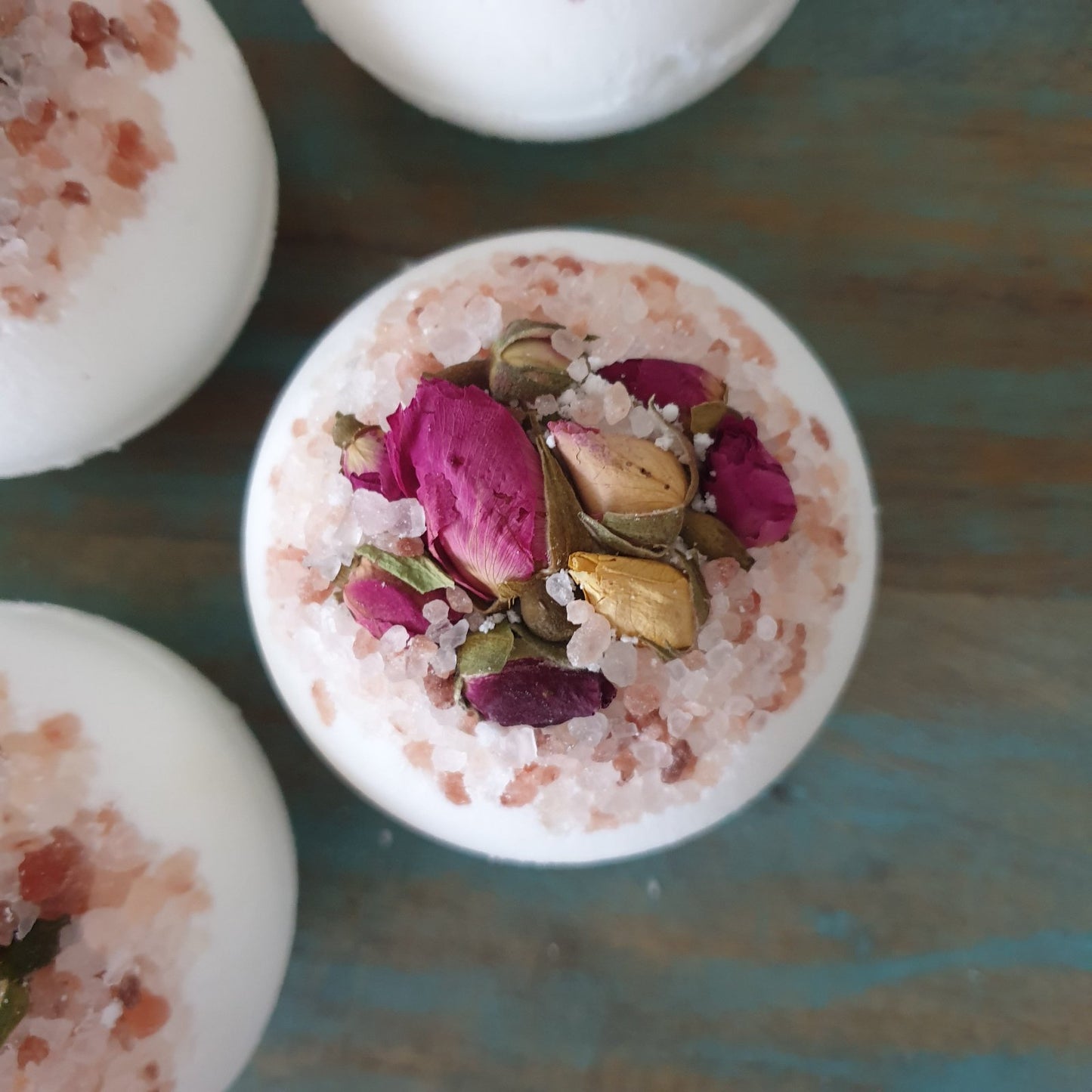 A beautifully staged photograph of the Blossom Secret Bath Bomb with dried rose buds and pink himalayan salt.