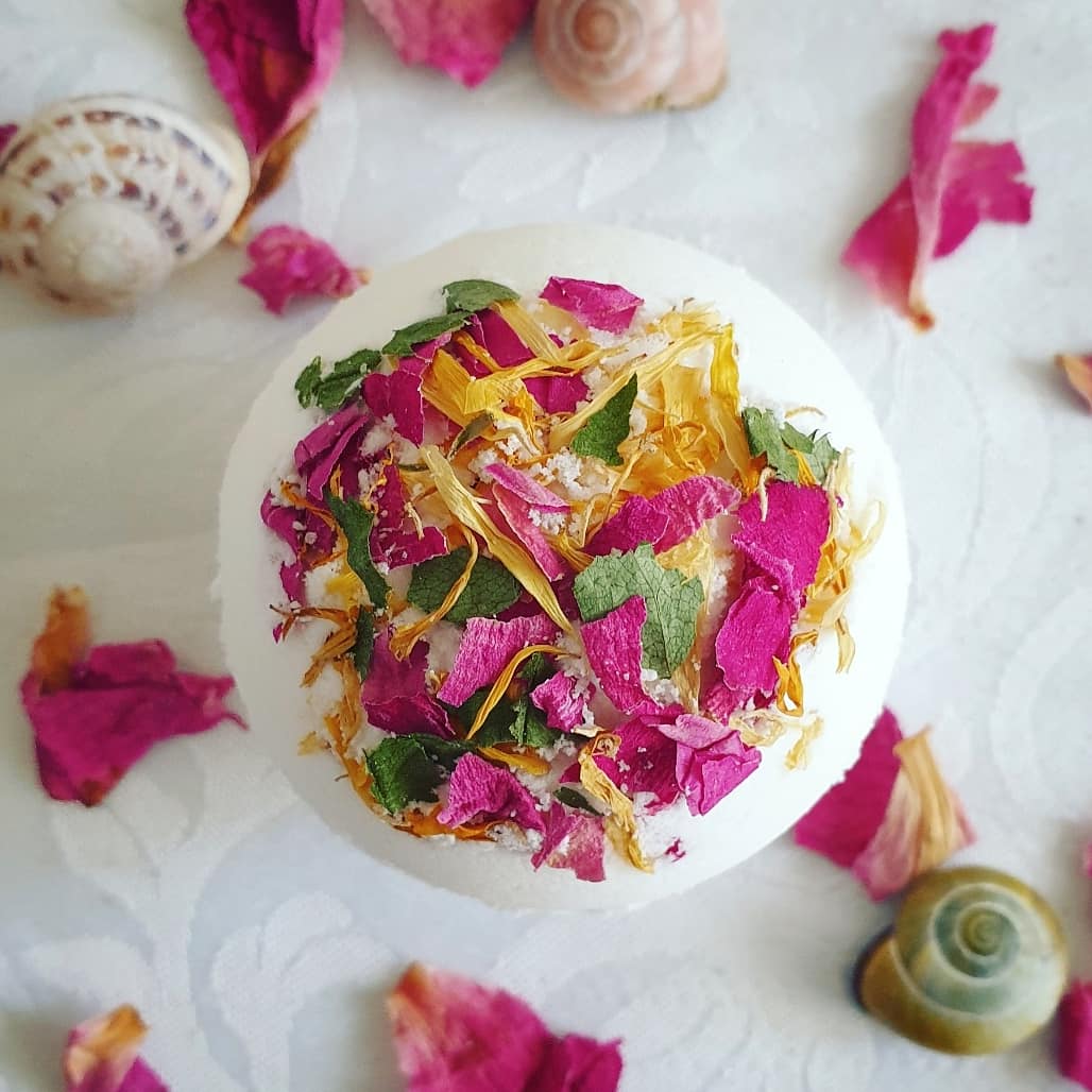 The Floral Relief Secret Bath Bomb, showcased alongside flower petals and seashells.