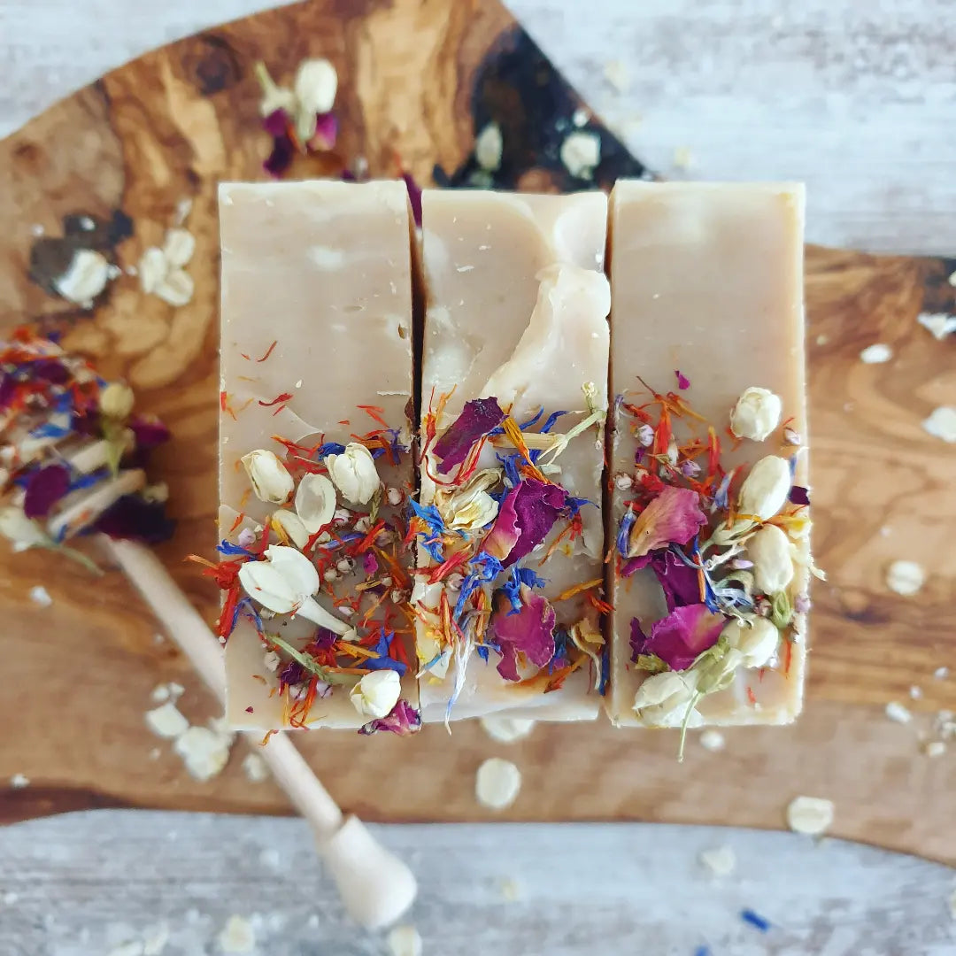 Three of The Eden Collections natural Honey and Oat Soap. Showcased on a wooden board sprinkled with oats and dried botanicals.