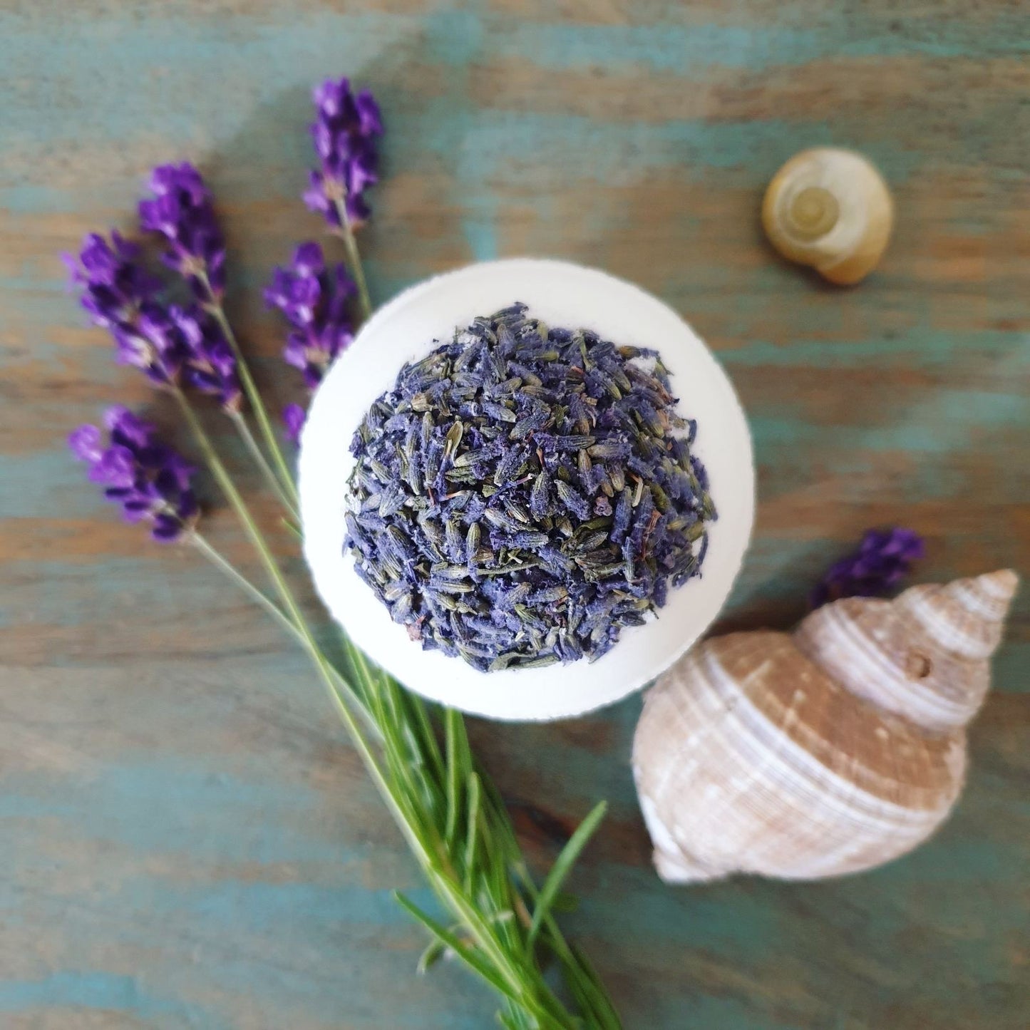 The nourishing skincare Lavender Secret Bath Bomb, displayed alongside lavender and seashells. Handmade by The Eden Collections