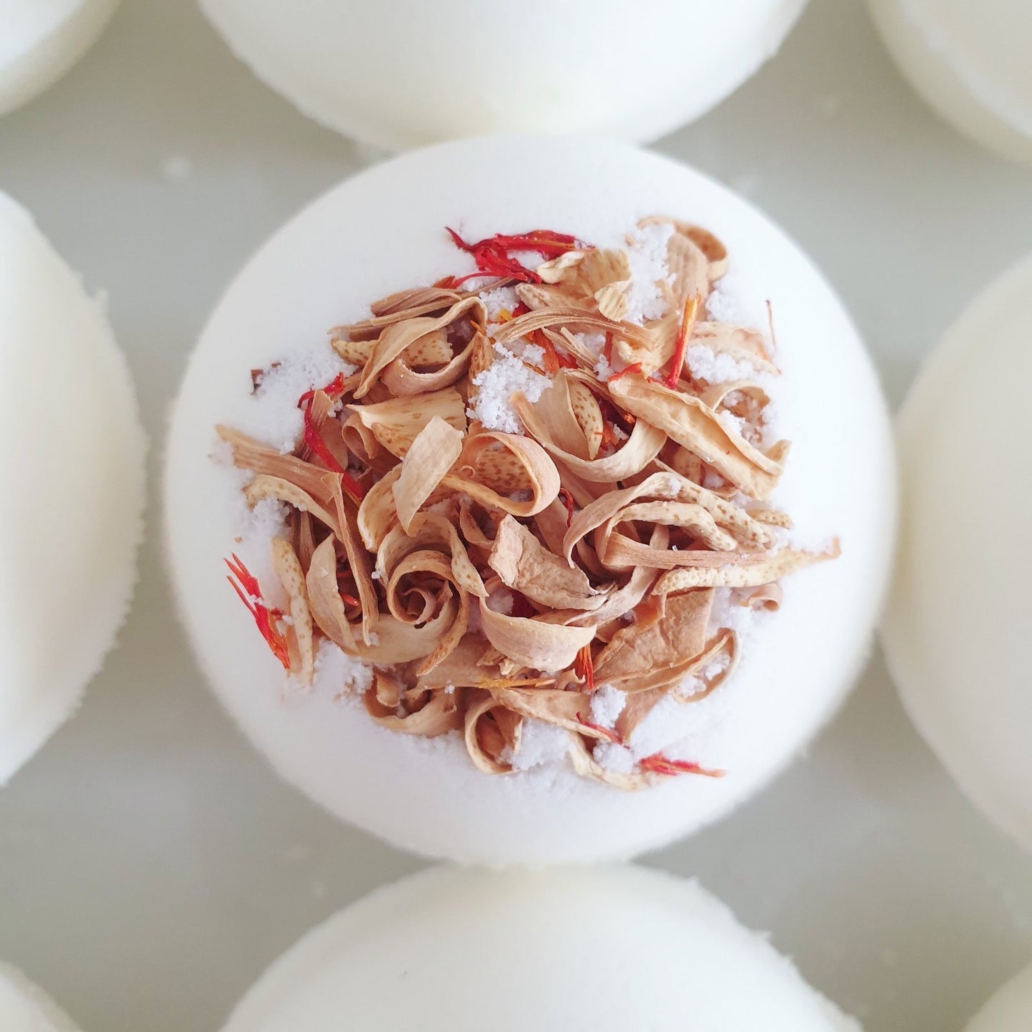 A close up photograph of The Eden Collections Orange Chocolate Secret Bath Bomb, showcasing the dried orange flower petals embedded into the top of this natural bath bomb.