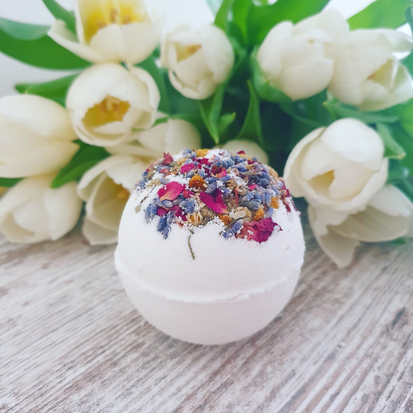 A side on view of the all natural Sweet Dreams Secret Bath Bomb, displaying the dried petals encased in the top of the bath bomb.