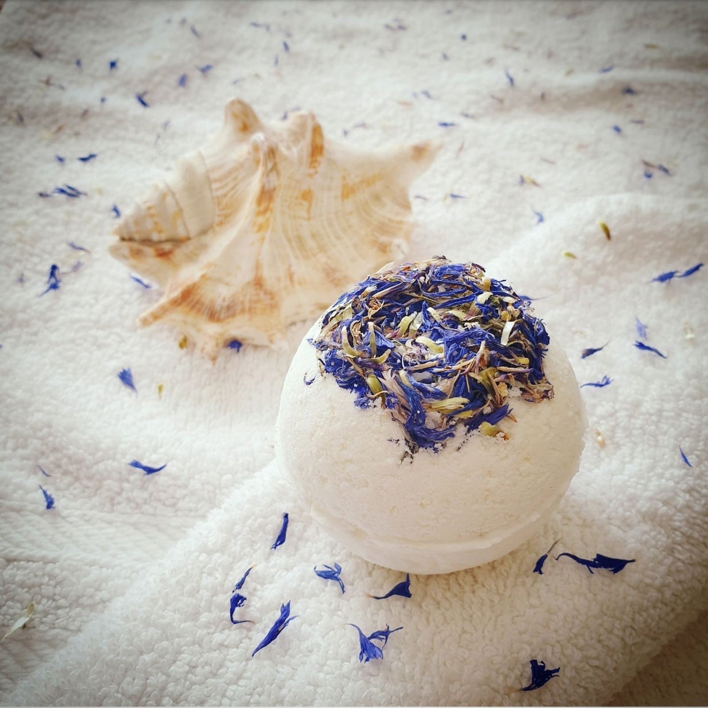 A side view of The Eden Collections Three Butters Secret Bath Bomb, highlighting the size of the bath bomb and the dried flowers encased in the top of the bath bomb.