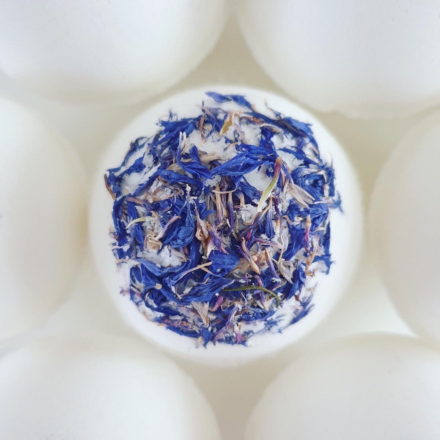 Three Butters Secret Bath Bomb, photographed from the top, decorated with blue cornflower. This unscented, organic bath bomb holds a hidden message inside and handmade by The Eden Collections.