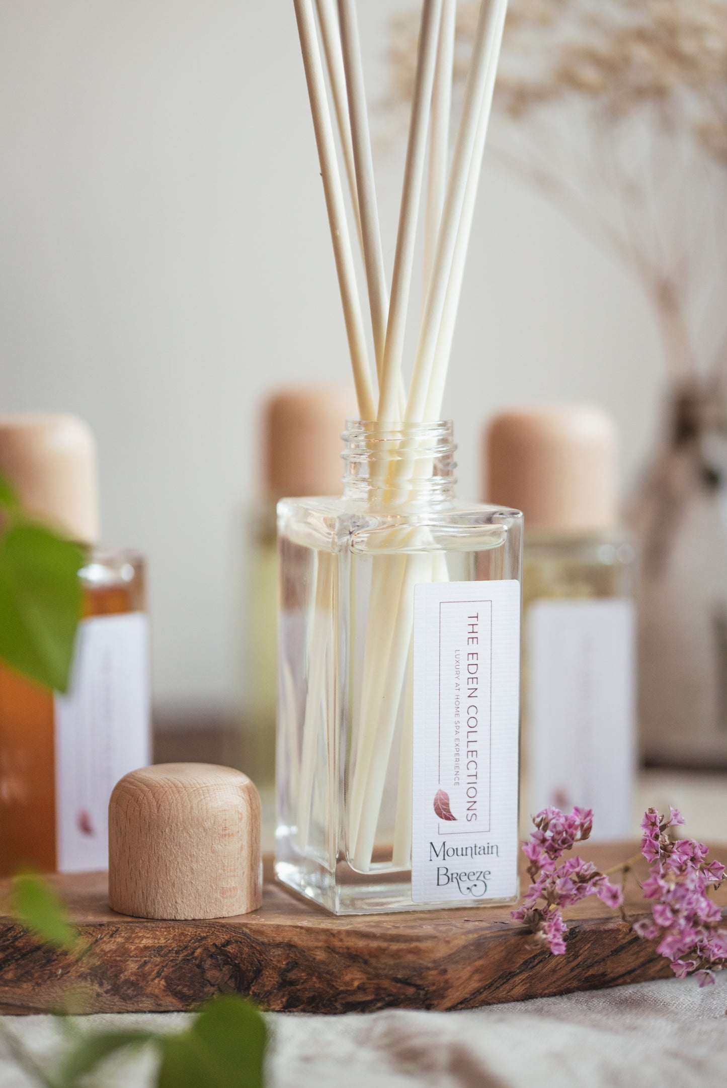 Elegant reed diffuser in a square glass jar with wooden cap. This essential oil reed diffuser is hand poured by The Eden Collections.