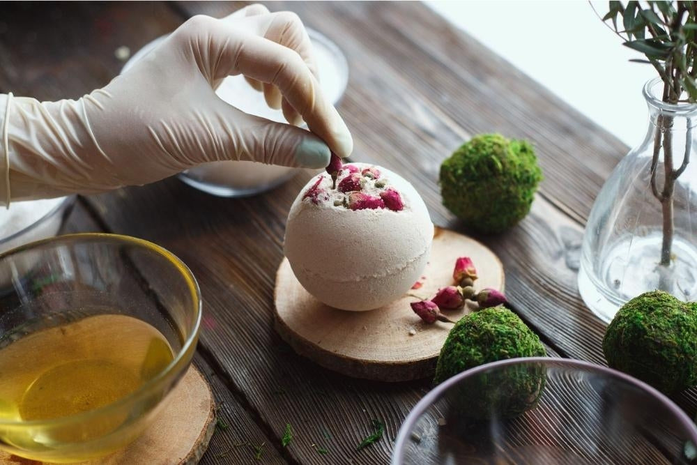 The ingredients of The Eden Collections Secret Bath Bombs, laid out on a wooden worktop, featuring a rose secret bath bomb.