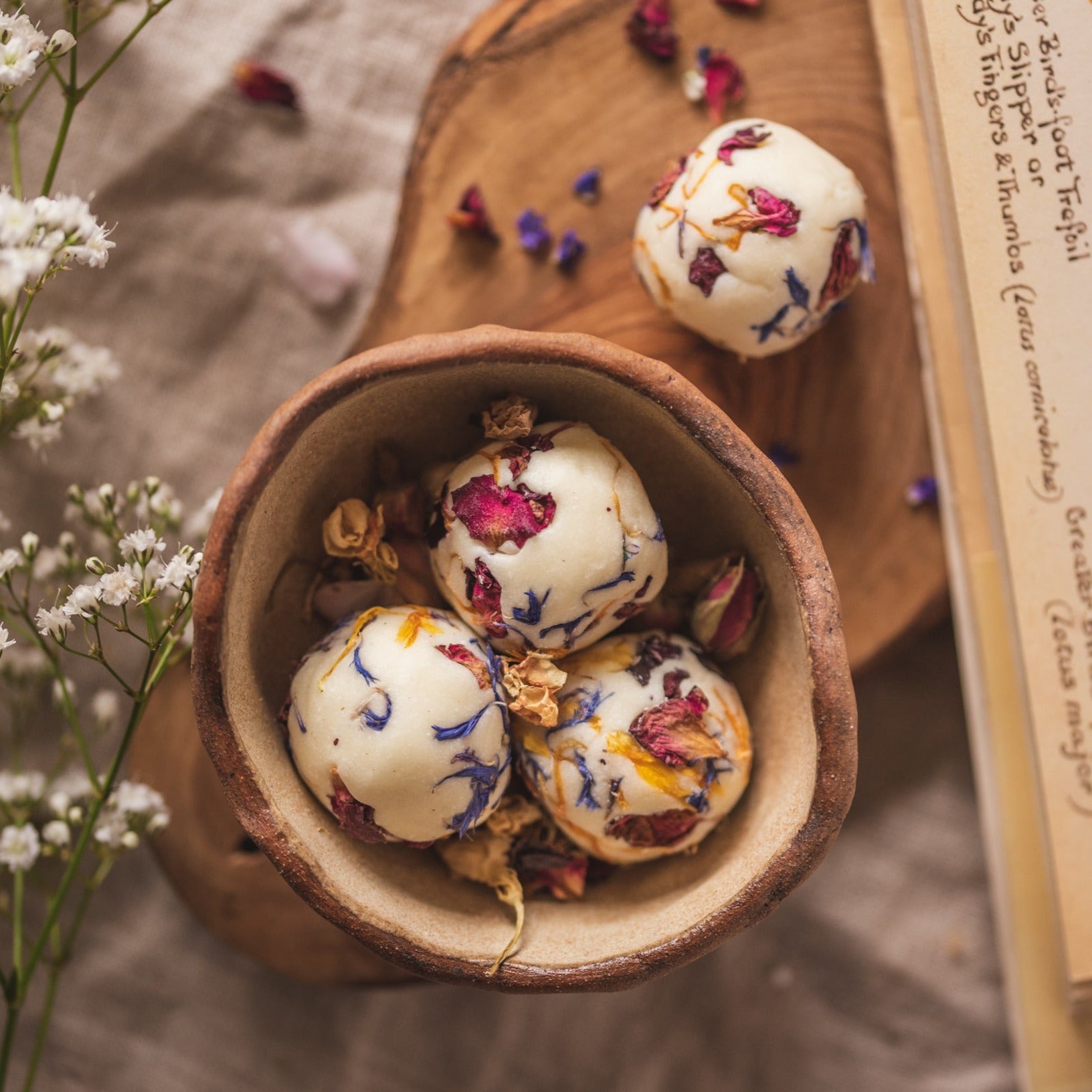 Four bath creamers by The Eden Collections, decorated with dried botanicals. The bath creamers are placed in a wooden bowl and showcased among baby breath flower and old book.