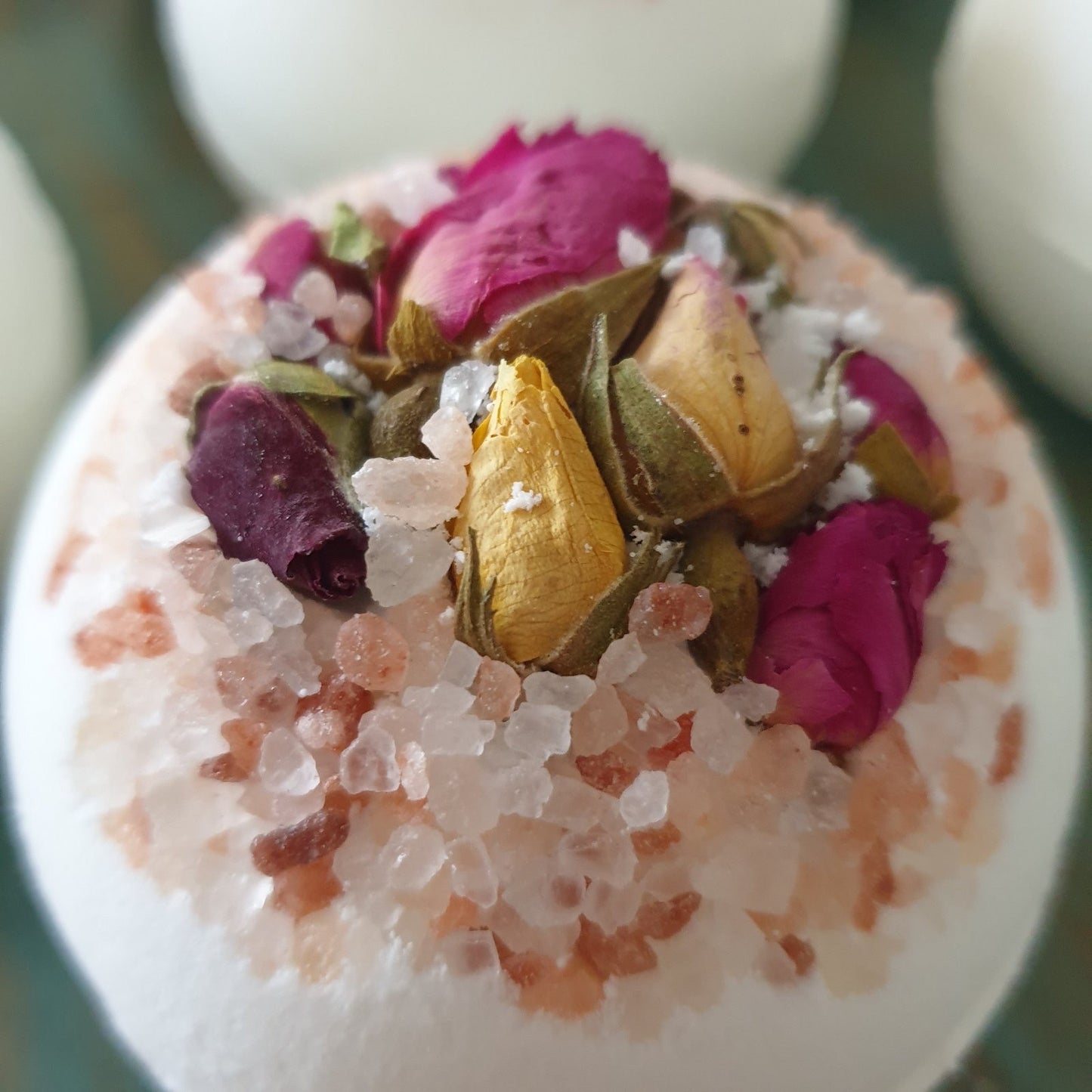 A close up photograph of the Blossom Secret Bath Bomb, showcasing its natural beauty with dried flower petals and organic salts.