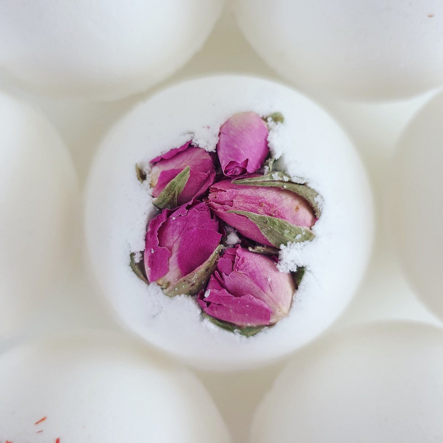 Rose Secret Bath Bomb, decorated with pink dried rose buds. Photographed from the top to showcase its beauty. Handcrafted by The Eden Collections