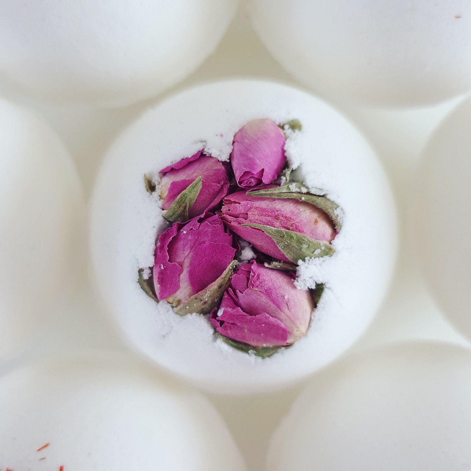 Rose Secret Bath Bomb, decorated with pink dried rose buds. Photographed from the top to showcase its beauty. Handmade by The Eden Collections, filled with organic butters, scented with essential oils.