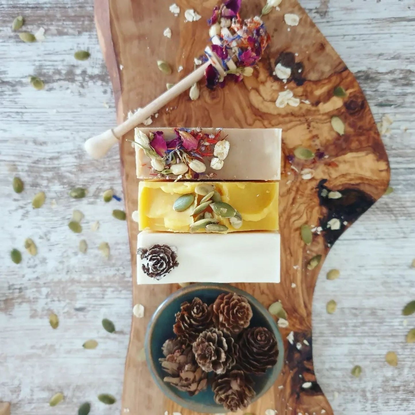 Winter Woods Soap, Cinnamon Spa Soap, and Honey & Oat Soap, lined up against one another, surrounded by pinecones, oats, and pumpkin seeds to represent The Eden Collections winter and autumn range.