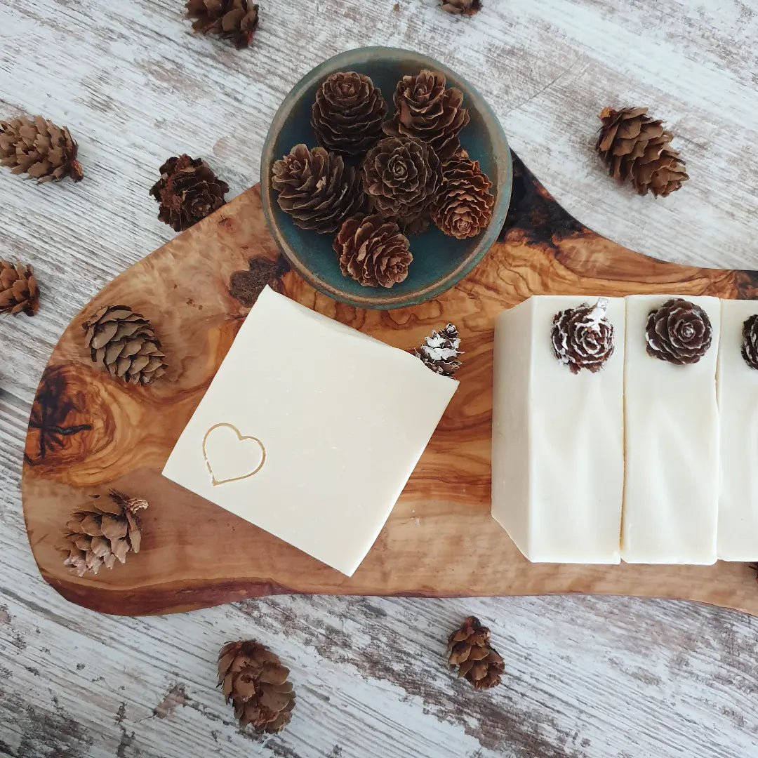 A collection of The Winter Woods Soap, showcased on a wooden board alongside a bowl of pinecones to represent the feel of winter. 